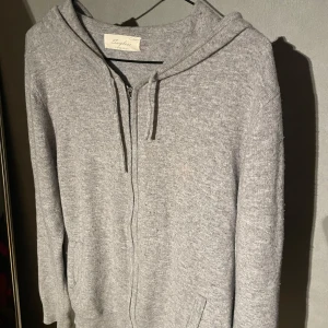 Grå cashmere hoodie  - Mjuk och lyxig grå hoodie i cashmere. Tröjan har dragkedja framtill, huva och långa ärmar. Perfekt för en avslappnad och stilren look. 