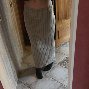 Beige ribbad långkjol - Säljer en beige ribbad långkjol med låg midja och rak passform. Kjolen är stickad och har ett stilrent, tidlöst utseende som passar perfekt till både sneakers och boots.