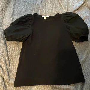 Svart topp med puffärmar från H&M - Säljer en svart topp från H&M med trendiga puffärmar och rund halsringning. Toppen har en stilren design och är perfekt för dig som gillar en enkel men ändå statement look.