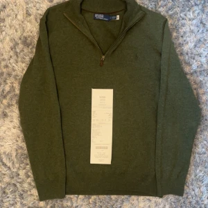 Olivgrön halvzip tröja från Polo Ralph Lauren - Snygg olivgrön tröja från Polo Ralph Lauren med halv dragkedja och ribbad krage. Klassisk broderad logga på bröstet. Perfekt för lager-på-lager och passar till det mesta. Materialet känns mjukt och håller värmen bra.