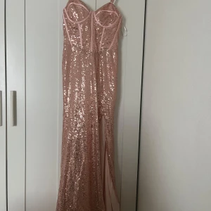 Rosa glittrig balklänning från Hebeos - Säljer en superfin rosa långklänning från Hebeos med paljetter över hela klänningen. Klänningen har smala axelband, markerad byst och en hög slits framtill. Perfekt för dig som vill sticka ut på festen!
