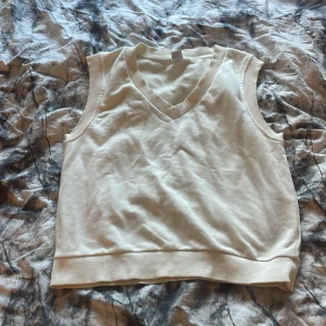 Vit v-ringad väst - Snygg beige väst med v-ringning och breda ribbade kanter. Perfekt att styla över en skjorta eller t-shirt för en trendig look. Kan förekomma någon liten fläck någonstans men bör gå bort i tvätten innan jag skickar iväg den!