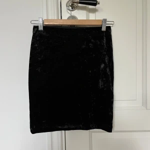 Svart sammetskjol - En svart sammetskjol med rak passform och kort längd. Kjolen har en enkel och stilren design utan synliga detaljer eller mönster. Perfekt för dig som gillar en klassisk look.