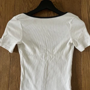 Vit ribbad topp med svarta kanter från Pimkie - Vit ribbad topp med svarta kanter från pimkie. Djup ringad längs ryggen, perfekt för att visa dina snygga ryggmuskler. Sitter tight