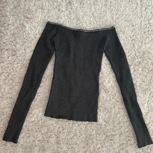 Mörkgrå ribbad offshoulder-tröja med pärlor från H&M - I väldigt bra skick. Säljer en mörkgrå ribbad offshoulder-tröja från H&M. Tröjan har långa ärmar och pärldetaljer längs halsringningen. Snygg och figurnära modell som passar perfekt till många olika outfits.