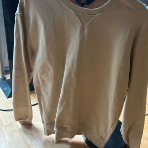 Beige sweatshirt från wacay - Säljer en beige sweatshirt från wacay med rund halsringning och lång ärm. Tröjan har en diskret patch med logga på ena ärmen och är tillverkad i mjuk bomull. Perfekt för en avslappnad och stilren look.