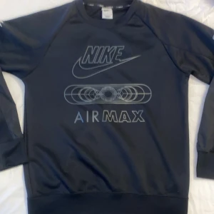 Svart Nike Air Max sweatshirt - Svart sweatshirt från Nike med Air Max-tryck på bröstet och loggor på båda ärmarna. Tröjan har rund halsringning och långa ärmar med paneldetaljer. Perfekt för en sportig och avslappnad stil.