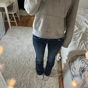 Mörkblå jeans - Säljer ett par mörkblå jeans med vita kontrastsömmar och snygga detaljer på bakfickorna. Byxorna har låg midja och klassisk femficksdesign. Passformen är slim och de sitter tajt längs benen.