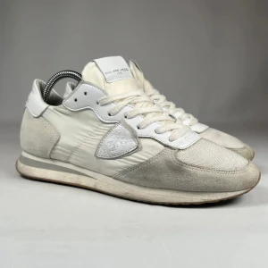 Vita sneakers från Philippe Model - Snygga vita sneakers från Philippe Model med paneler i mocka och textil. Skorna har snörning, rund tå och platt sula. Perfekta för en stilren och sportig look.
