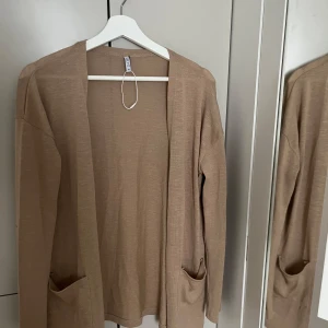 Beige kofta i xs - Säljer en tunn och enkel beige kofta från SAILS. Koftan har långa ärmar och två fickor framtill. Perfekt att slänga över en topp för en avslappnad look.