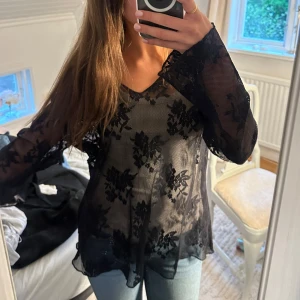 Svart blommig spetsblus - Säljer en transparent svart blus i spets med blommigt mönster. Blusen har långa ärmar och v-ringad halsringning. Perfekt för dig som vill ha en snygg och trendig topp🥰