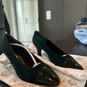 Mörkgröna pumps med lackad tå från Bruno Magli  - Snygga mörkgröna pumps med klack och lackad spetsig tå. Skorna har en elegant form och är tillverkade i mocka med detaljer i lack. Perfekta för dig som vill ha en klassisk och stilren sko med det lilla extra. Skulle att det är en stor i storleken, passar strl. 38💚