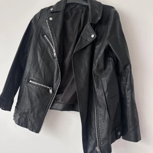 Svart skinnjacka med dragkedjor - Säljer en svart skinnjacka med coola silverfärgade dragkedjor och klassisk krage. Jackan har snedställd dragkedja framtill och detaljerade fickor. Perfekt för dig som vill ha en edgy stil.