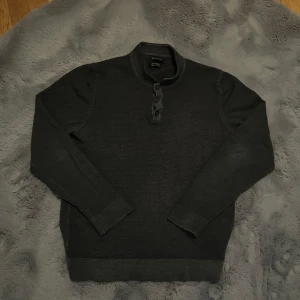 Grå merinoullströja från Massimo Dutti - Säljer en grå långärmad tröja i 100% merinoull från Massimo Dutti. Tröjan har ståkrage och tre knappar framtill för en stilren look. Perfekt för dig som gillar klassisk och enkel stil.