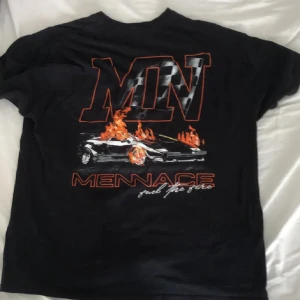 Svart t-shirt från Mennace med tryck - Svart t-shirt från Mennace med stort grafiskt tryck på ryggen av en bil i eld och texten 'MN' och 'MENNACE'. Framtill finns en mindre logga och text. Klassisk passform och rund hals.