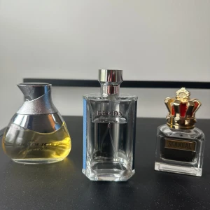 Tre exklusiva parfymer från olika märken - Säljer tre parfymer: en med rund guldfärgad flaska och silverlock, en rektangulär flaska från Prada med metallock, samt en fyrkantig flaska med gulddetaljer och röd krona på locket från Scandal. Perfekta för dig som gillar lyxiga dofter.
