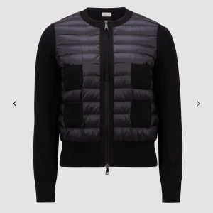 Svart puffer cardigan jacka från Moncler - Säljer en svart cardigan jacka från Moncler med puffer-detaljer framtill och stickade ärmar. Jackan har dragkedja och två fickor framtill. Perfekt för lager-på-lager och snygg till både jeans och kjol.