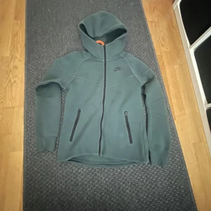 Grå hoodiejacka från Nike - Mörkgrå hoodiejacka från Nike med hel dragkedja och två fickor med dragkedja framtill. Köpt på JD för något år sen. Nästan nyskick använd 2-3 gånger. Obs(Det är inte en Nike tech fleece det är en Nike tech hoodie) Tror dock inte att någon säljer dem längre dock.