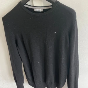 Svart tröja från J.Lindeberg - Klassisk svart tröja från J.Lindeberg med rund halsringning och diskret logga på bröstet. Långärmad modell i 100% merinoull , perfekt för en stilren look. Tröjan har krympt i tvätten och passar mer som S, märks inget på materialet.