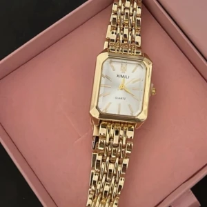 Guldig fyrkantig klocka  - Stilren klocka  med fyrkantig urtavla i vitt och detaljer i guld. Armbandet är länkformat och helguldigt, vilket ger en lyxig känsla. Perfekt accessoar för att lyfta din outfit.
