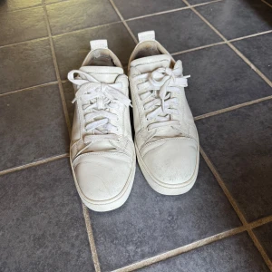 Christian Louboutin - Snygga vita sneakers från Christian Louboutin i skinn med klassiska röda sulor och snörning. Stilren design med rund tå och platt sula, perfekta för dig som vill ha en clean look med en lyxig touch. Kvitto finns.