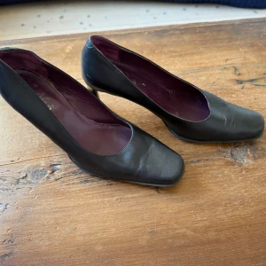 Svarta pumps med fyrkantig tå - Stilrena svarta pumps i skinn med fyrkantig tå och låg klack. Insidan är fodrad i mörklila, vilket ger en snygg kontrast. Perfekta för dig som gillar klassisk och minimalistisk stil med en twist. Storlek 37,5. 