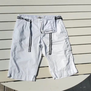 Vita shorts från Hampton Republic - Snygga vita shorts från Hampton Republic med svartvitt knytskärp i midjan. Klassisk rak modell med fickor fram och bak, samt dragkedja. Perfekta för sommardagar och chill häng. Tunn bomullskvalitet som känns lätt och luftig.