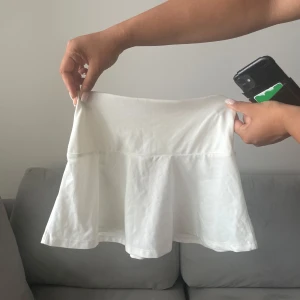 Vit kort, ”tenniskjol” med rynkdetalj - Supersöt vit kortkjol med lätt utsvängd form och rynkdetalj baktill i midjan. Kjolen är enkel och stilren, perfekt till sneakers eller sandaler. Tillverkad i mjukt bomullstyg som känns skönt mot huden. Passar dig som gillar en clean och fräsch look.