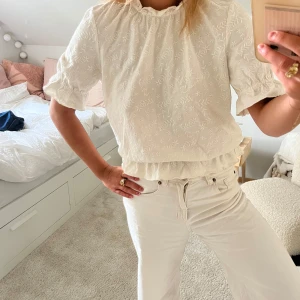 Vit broderad blus från & Other Stories - Superfin vit blus från & Other Stories med broderade blommor och volangdetalj nertill. Blusen har korta ärmar med resår och en lätt rynkad halsringning. Perfekt för dig som gillar romantiska och luftiga toppar med extra detaljer.