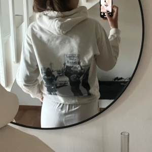 Vit hoodie med tryck på ryggen - Säljer en benvit hoodie med huva och tryck på ryggen. Hoodien är i mjuk bomull och har en avslappnad passform, fint skick.