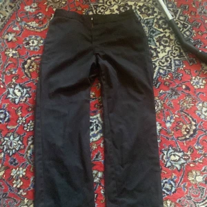 Svarta Dickies 874 byxor - Klassiska svarta Dickies 874 Original Fit byxor med raka ben och normal passform. Byxorna har bälteshällor, dragkedja och knapp framtill samt två bakfickor. Perfekta för en clean och stilren look.