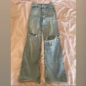 Blå bootcut jeans från Zara - Säljer ett par ljusblå bootcut jeans från Zara i storlek 34. Jeansen har hög midja och hål vid knäna.