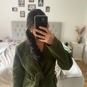 Olivgrön kappa med bälte - Säljer en olivgrön lång kappa som är perfekt för hösten och vintern! Stilig och inga tecken på användning!! Funkar som både XS/S och M. Nypris 1000 säljer för 500
