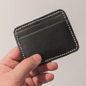 Svart skinnplånbok med vita sömmar - Minimalistisk svart plånbok i skinn med kontrasterande vita sömmar runt kanterna. Plånboken har flera kortfack och en stilren, enkel design som passar perfekt i fickan. Perfekt för dig som vill ha koll på korten utan att ta plats.