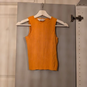 Ribbad orange linnetopp - Säljer en ribbad orange linnetopp. Toppen är ärmlös med rund halsringning och har en tight passform. Perfekt för att ge din outfit en färgklick och funkar lika bra till jeans som kjol.