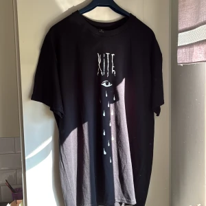 Svart KITE t-shirt med tryck XL - Svart t-shirt från Gildan i heavy cotton med tryck framtill: texten KITE ovanför ett öga med tårar. Klassisk passform och rund hals. Perfekt för dig som gillar grafiska prints och vill sticka ut lite extra. Aldrig använd 