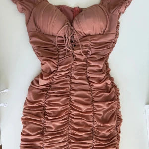 Rosa kortklänning från Love Triangle - Supersöt kortklänning i dammigt rosa färg från Love Triangle. Klänningen har snygg snörning framtill, vadderad byst och är täckt av trendiga rynkade detaljer. Tillverkad i ett lätt, mesh-liknande syntetmaterial och har dragkedja i ryggen. Köpte den för ungefär 1 år sedan och använt den bara en gång till en studentfest. Ord pris 349kr, pris kan diskuteras.