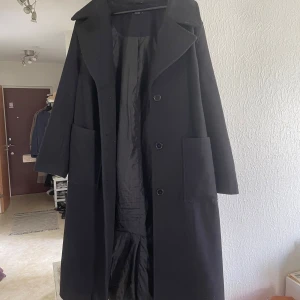 Svart kappa - Stilren svart kappa förmodligen från Kappahl då dom säljer kläder av Xlnt. Stora fickor, ganska bred krage och knappar. Kappan har ett bälte i midjan för en snygg siluett. Varm nog för hösten och mild vinter. Funkar även till 38/M skulle jag säga