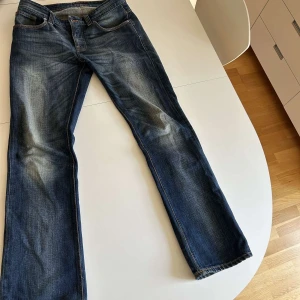 Tvättade nudie jeans - Säljer ett par klassiska blå jeans från Nudie med snyggt slitna detaljer och kontrastsömmar. Modellen har bootcut-ben och coola broderade bakfickor med Nudie-loggan. Jeansen är i kraftigt denimtyg och har en autentisk vintagekänsla. W32 L34