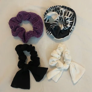 Scrunchies i olika färger - Fyra scrunchies: en glittrig lila, en med svart-vitt-blått mönster, en svart med rosett och en vit med rosett. Köp alla för 35kr eller en för 10kr