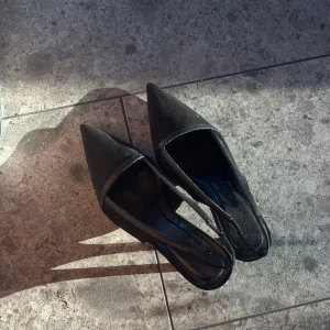 Svarta pumps med spetsig tå - Stilrena svarta pumps med spetsig tå och öppen häl. Skorna har en elegant form och är tillverkade i mocka med detaljer i skinn. Perfekta för dig som gillar en klassisk och trendig look och perfekt för alla tillfällen!! 😍😍 