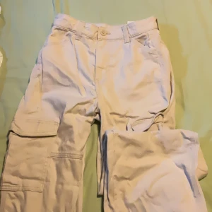 Beiga cargopants från H&M Divided - Säljer ett par beiga cargopants från H&M Divided i 100% bomull. Byxorna har flera stora fickor på benen och klassisk cargostil. Perfekta för en chill och avslappnad look. Passar dig som gillar praktiska och trendiga byxor.
