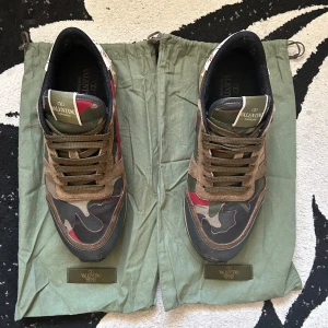 Valentino Rockrunners - Snygga Valentino Rockrunner sneakers med ikoniskt camouflagemönster i grönt, brunt, svart och röda detaljer. Skorna har partier i mocka och skinn, samt coola nitar på hälen och broderad detalj på baksidan. Perfekta för dig som vill sticka ut med stil.