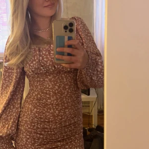 Blommig kortklänning med puffärm - Supersöt kortklänning  med vita blommönster. Klänningen har långa puffärmar med resår vid handlederna och smickrande rynkdetaljer längs kroppen. Perfekt för vår och sommar, ger en romantisk vibe.