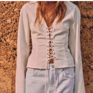 Vit korsettopp med snörning💖💖 - Supersnygg vit korsettopp med lång ärm och djup v-ringning. Toppen har cool snörning framtill som ger en edgy vibe och markerar midjan. Perfekt att styla med jeans eller kjol för en trendig look.