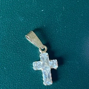 Liten korsberlock i guld och kristall - Säljer en liten och stilren korsberlock i guld med gnistrande stenar stämpel 750 Perfekt att hänga på ett halsband . Korset har en klassisk form och detaljerad. Köptes på guldfynd för nåt år sen. 