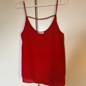 Röd linnetopp från Pieces - Säljer en röd linnetopp från Pieces i storlek S. Toppen har tunna axelband, v-ringad hals och dubbla lager tyg nedtill för en snygg flowy look. Perfekt för dig som gillar enkel men stilren design med en poppig färg.