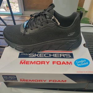 Svarta sneakers från Skechers - Svarta sneakers från Skechers med chunky sula och memory foam för extra komfort. Ovandelen är i stickad syntet med diskreta detaljer och snörning. Perfekta för dig som vill ha en sportig och stilren look med maximal dämpning.