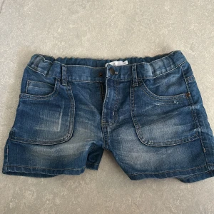 Blå jeansshorts från Åhléns - Snygga blå jeansshorts från Åhléns med klassisk femficksdesign, resår i midjan och slitna detaljer framtill. Shortsen har knappar på bakfickorna och är perfekta för sommardagar. Sköna och lätta att matcha med allt.💕