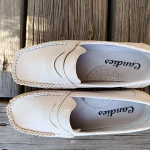 Beige loafers i skinn från Candice - Snygga beige loafers från Candice i konst skinn med klassisk penny loafer-design. Skorna har sydda detaljer runt tån och en platt, räfflad sula i gummi för extra grepp. Perfekta för en clean och stilren look. Begagnad skick, se bilder.